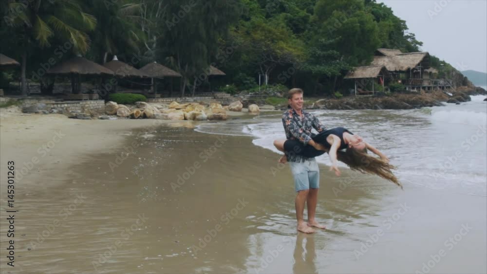 A man holds a woman in his arms, a young couple in love swirl on the sea beach in slow motion. The concept of a happy family and rest A man holds a woman in his arms, a young couple in love swirl on the sea beach in slow motion. The concept of a happy family and rest