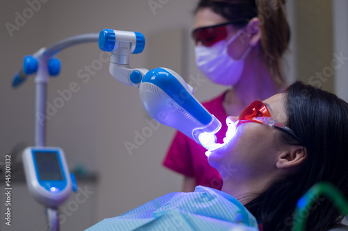 Close-up portrait of a female patient at dentist in the clinic. Teeth whitening procedure with ultraviolet light UV lamp. photo