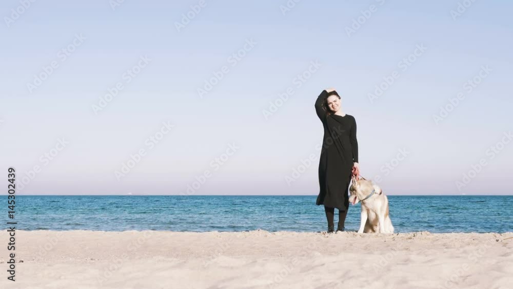 Young female standing with siberian husky dog with beach background Young female standing with siberian husky dog with beach background