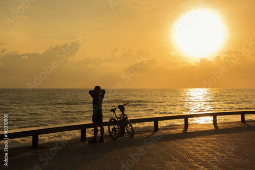 Single man warm down after riding bicycle in the park near the sea in morning ; Songkhla province, Thailand (Silhouette style)