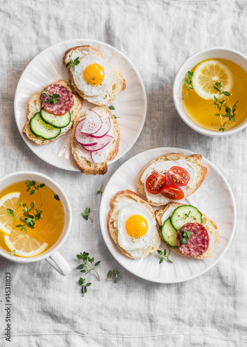 Delicious Breakfast - mini sandwiches with cream cheese, vegetables, quail eggs, salami and green tea with lemon and thyme.s, radish, thyme, lemon zest, fried quail eggs 