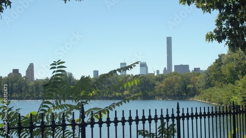 Tree branches revealing beautiful Jacqueline Kennedy Onassis Reservoir in green Central Park overlooking 432 Park Avenue condominiums and contemporary glassy skyscrapers in Manhattan Upper West Side