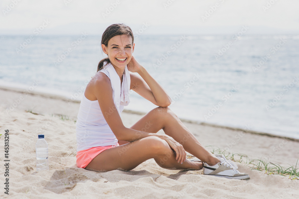 sporty woman smiling while sitting on the sand after workout