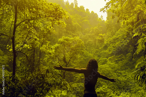 Man stays with his back in front of jungle and raise his hands to the sides. Freedom concept