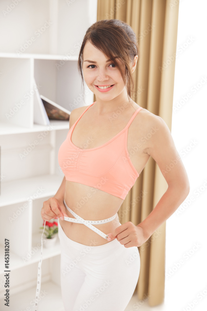 sporty woman smiling while measures her waist with measuring tap sporty woman smiling while measures her waist with measuring tap