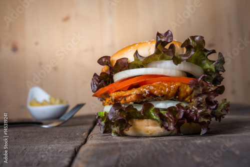 Home made chicken burger with French fries, lettuce, tomato and onion on wooden board.