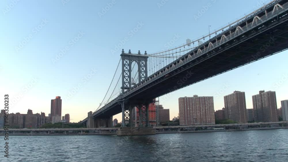 HYPERLAPSE LOW ANGLE VIEW Sightseeing cruise on East River under Manhattan Bridge along luxury waterfront condominium apartments in residential area of Lower Manhattan, New York City at golden sunset HYPERLAPSE LOW ANGLE VIEW Sightseeing cruise on East River under Manhattan Bridge along luxury waterfront condominium apartments in residential area of Lower Manhattan, New York City at golden sunset
