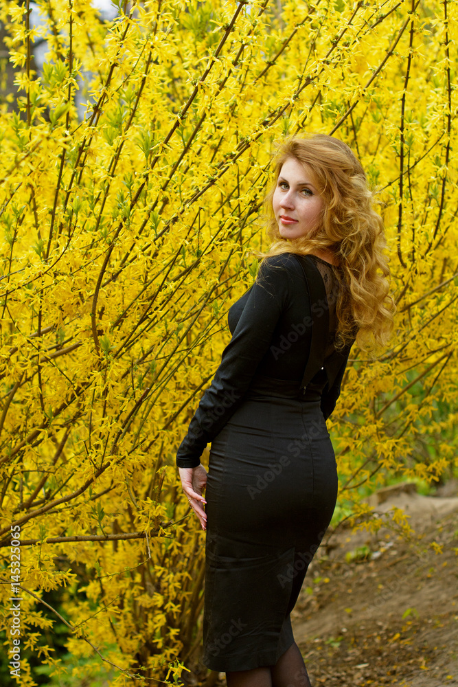 Attractive young sexy woman in a black dress in a botanical garden looks at a yellow plant that comes with a pleasant walk and a visit surrounded by plants