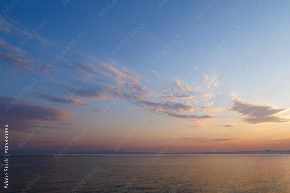 Fototapeta premium Early morning at dawn of the day with a calm blue sea overlooking the cloudy sky and mountains of the other shore