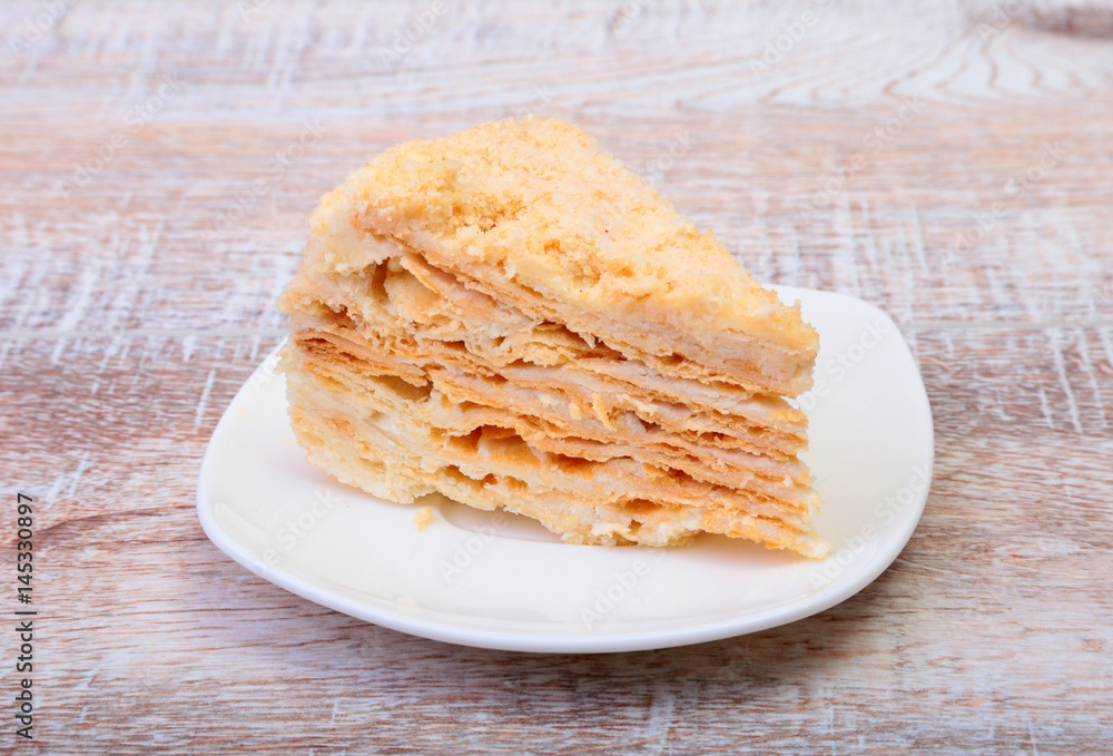 Homemade Napoleon puff cake on plate on wooden table close-up. Homemade Napoleon puff cake on plate on wooden table close-up.