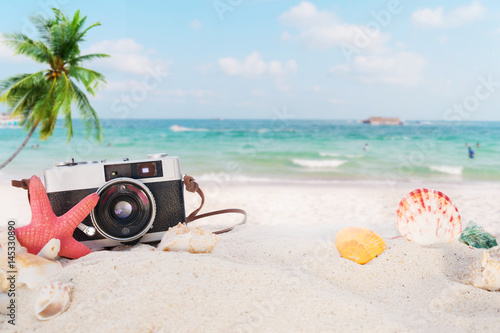 The concept of leisure travel in the summer on a tropical beach seaside. retro camera on the sandbar with starfish, shells, coral on sandbar and blur sea background. vintage color tone styles.