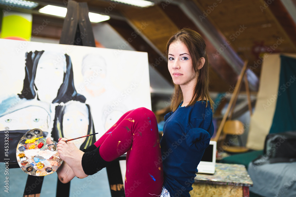 Obraz premium Disabled beautiful young artist painting incredible scenes in attic by holding paintbrush in her toes. 