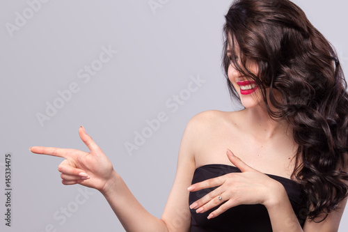 Happy woman with long and shiny wavy hair . Beautiful model, curly hairstyle on gray background showing on copy space.