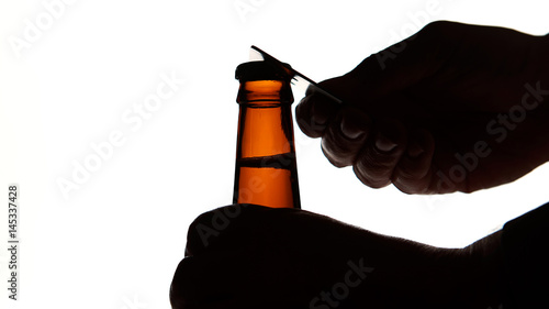 Silhouette of Male hands opening brown beer bottle with opener