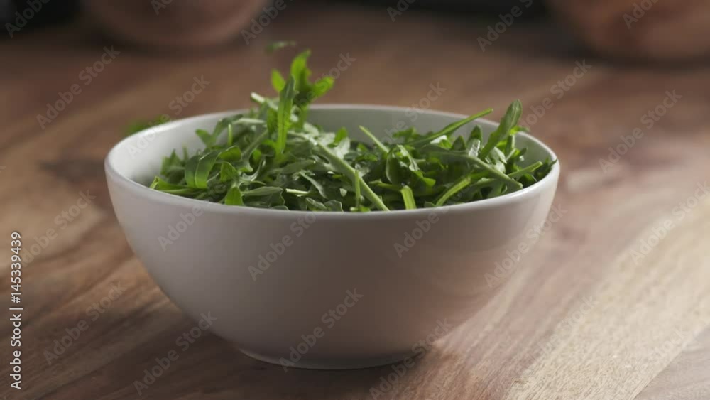 Slow motion of washed arugula leaves falling into the bowl on wooden table, 180fps prores footage Slow motion of washed arugula leaves falling into the bowl on wooden table, 180fps prores footage