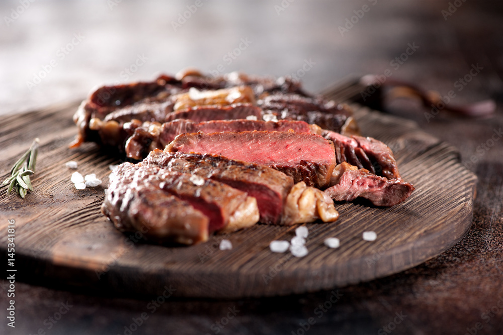 Ribeye steak slices with salt and rosemary on a wooden serving board Ribeye steak slices with salt and rosemary on a wooden serving board