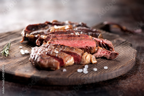 Fotografia Ribeye steak slices with salt and rosemary on a wooden serving board