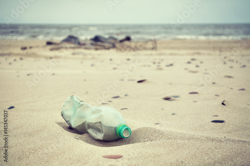 Retro stylized picture of an empty green plastic bottle left on a beach, selective focus, environmental pollution concept picture. 