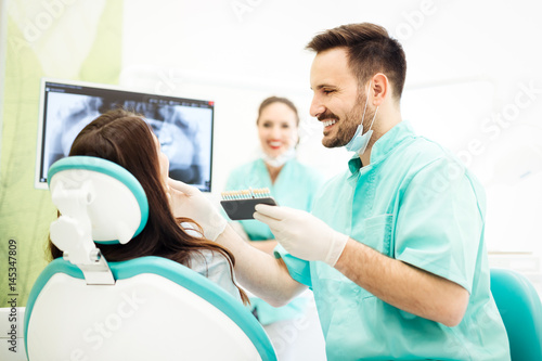 Dentist checking and selecting color of young woman s teeth