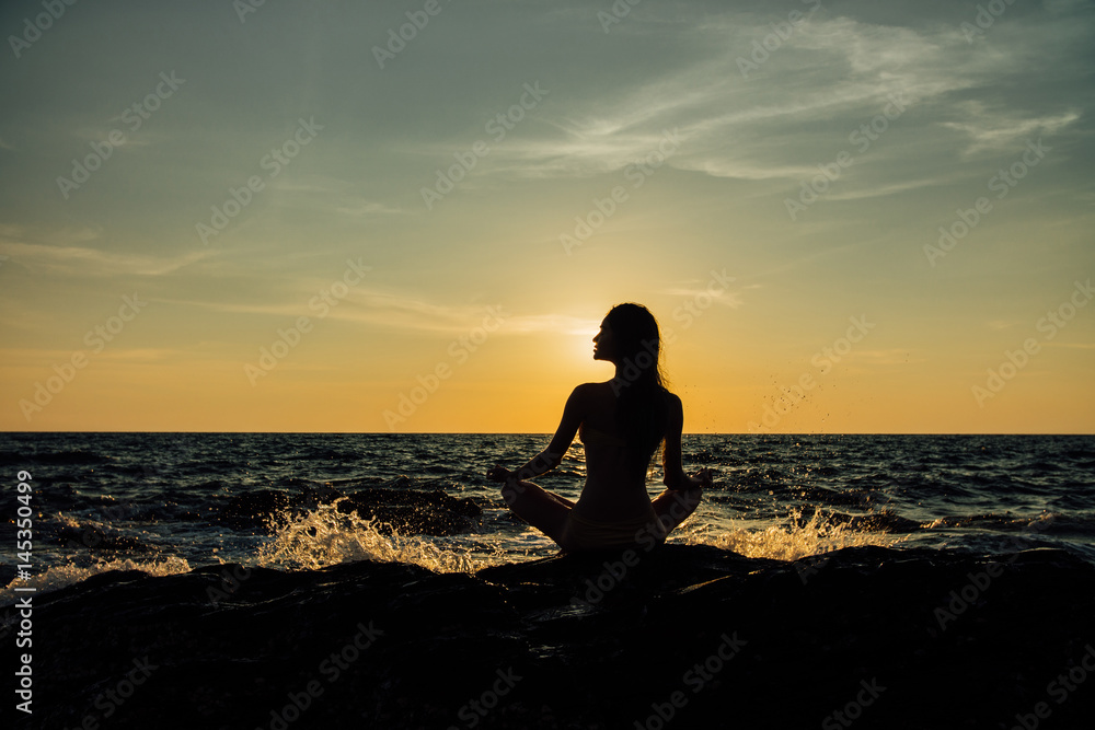 Silhouette meditation girl lotus position on stone on the background of the stunning sea.