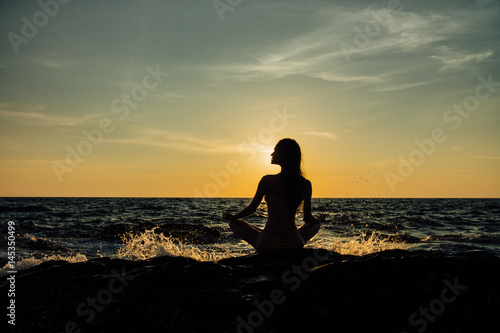 Silhouette meditation girl lotus position on stone on the background of the stunning sea. © photominus21