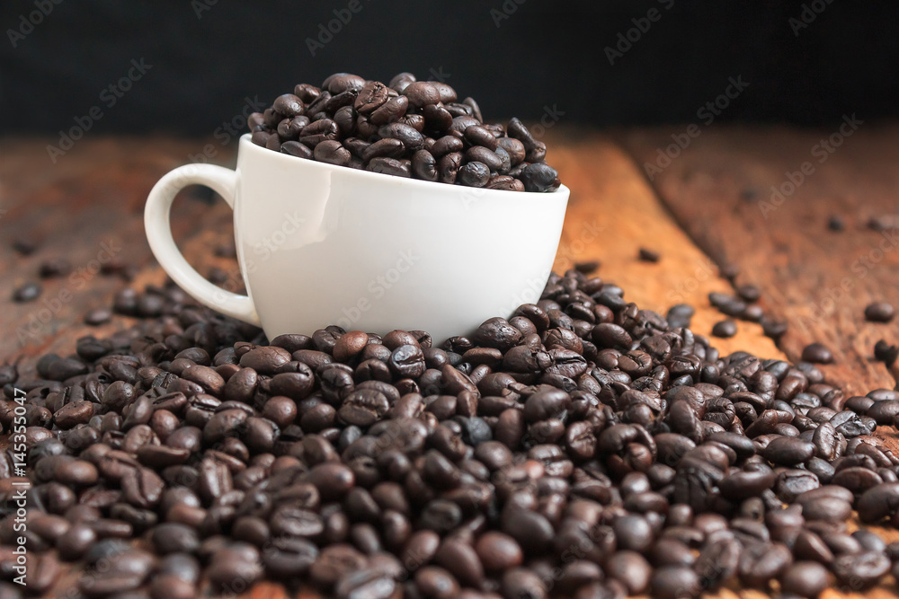 Fototapeta premium Close up shot of dark roasted coffee bean in white ceramic cup on wooden floor with copy space