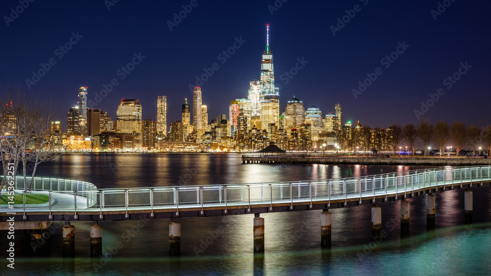 New York City Financial District skyscrapers and Hudson River from Hoboken promenade in evening. Lower Manhattan skyline and pedestrian bridge from New Jersey