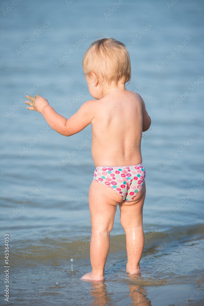Baby playing on the sandy beach and in sea water. Cute little kid with toys on sand tropical beach. Ocean coast.