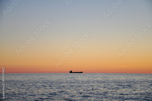 Sea at sunset far away can be seen the silhouette of the ship.