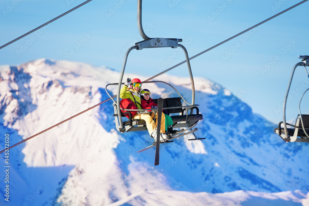 Two skiers lifting on lift against snowy mountains