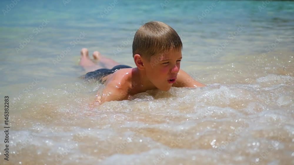 The child lies on the beach and swims in the sea waves on a sunny day The child lies on the beach and swims in the sea waves on a sunny day