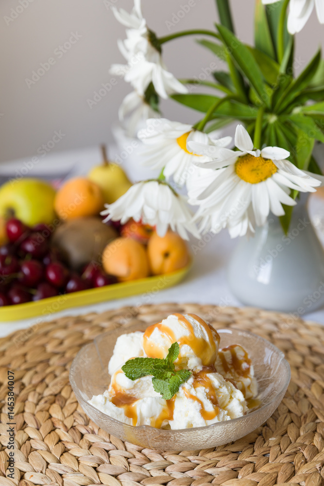 Homemade frozen yogurt or ice cream served with caramel. Delicious sweet dessert on the table with fruit background