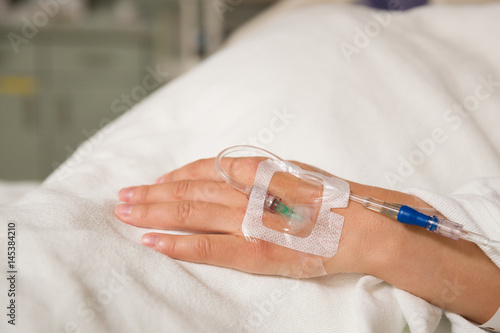 Close up hand of young patient with intravenous catheter for injection plug in hand during lying in the hospital bed. photo