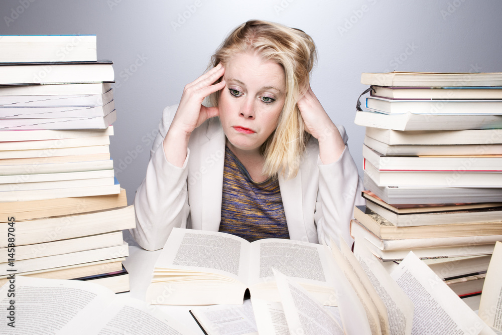 Young, blonde, attractive woman or student sitting tired at desk surrounded with books. Young, blonde, attractive woman or student sitting tired at desk surrounded with books.