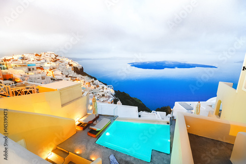 Swimming pool with torcouise water inside against Aegean sea and island in vista in Fira village at Santorini island, Greece, Europe. Santorini famous, popular sea resort with exquisite architecture.