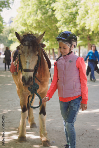 Young girl wearing jockey helmet and holding poney photo