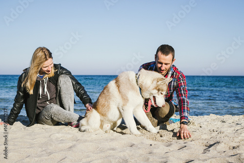 Young cute caucasian couple on beach with siberian husky dog