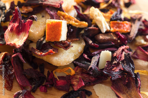 Pile of fruit tea with petals and dry fruit .The composition of the heap of tea leaves and dried hibiscus flower located on a wooden Board. Tea with natural ingredients closeup. Macro photo of tea.