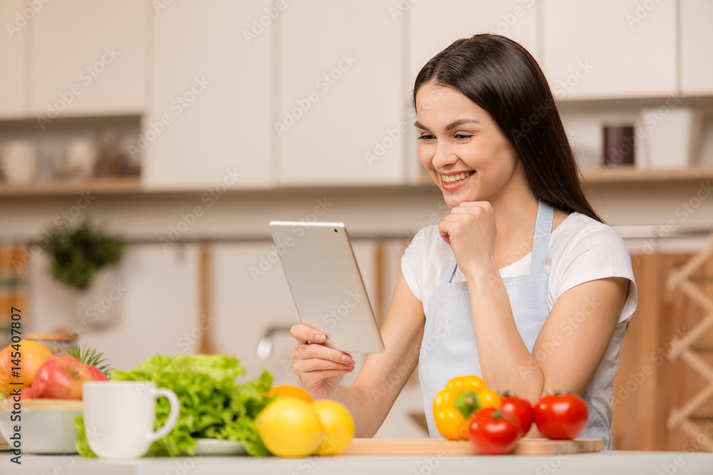 Young Woman standing in kitchen with tablet computer and looking recipes. Food blogger concept