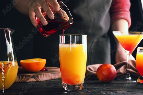 Woman making tequila sunrise cocktail in bar