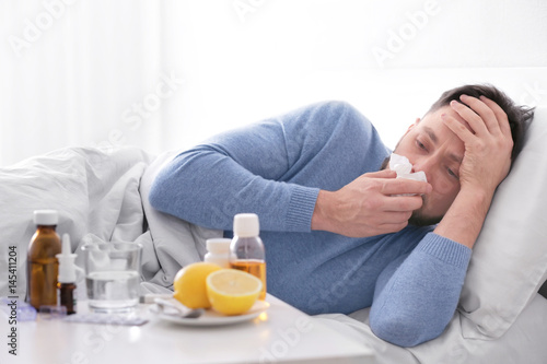 Foto Young ill man lying in bed at home