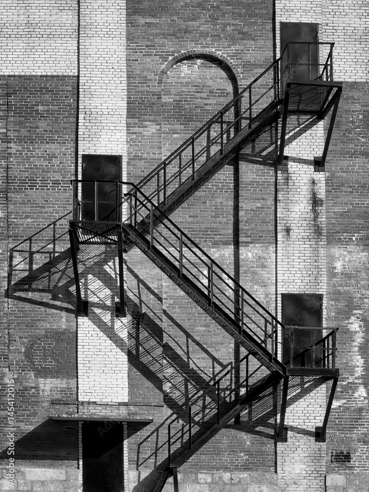 Steel stair and black doors on old industrial building brick wall. On direct hot sun.