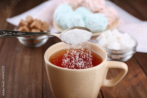 Canvas Print Adding sugar to cup of black tea on wooden table