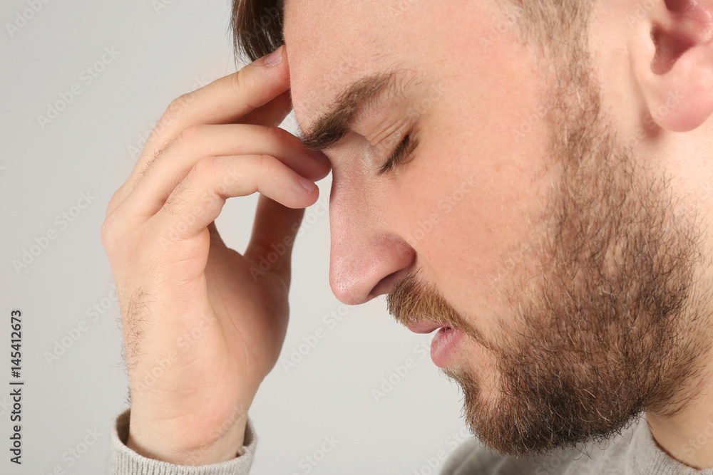 Obraz premium Young man suffering from headache on light background
