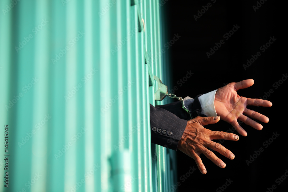 hands of business man locking with handcuff in jail as background.