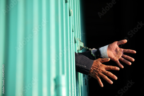 hands of business man locking with handcuff in jail as background.