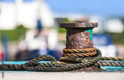 Fotografie An old, rusty bollard in a harbor by the sea