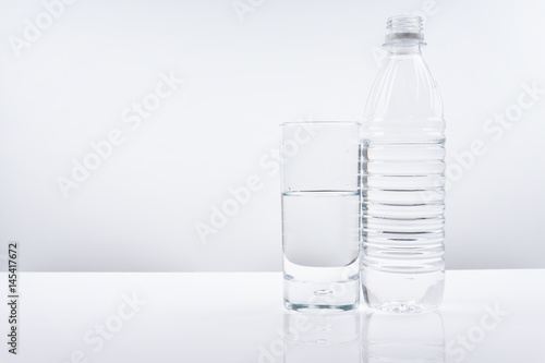 Plastic bottle and glass of mineral water on white background.