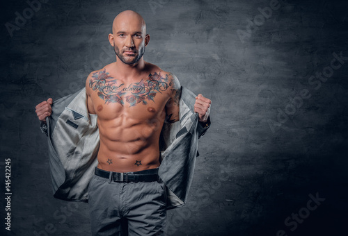 Slika na platnu Shaved head tattooed male dressed in a grey jacket on a naked torso