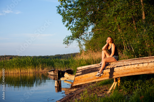 Летним днем ​​девушка сидит на лодке на берегу озера